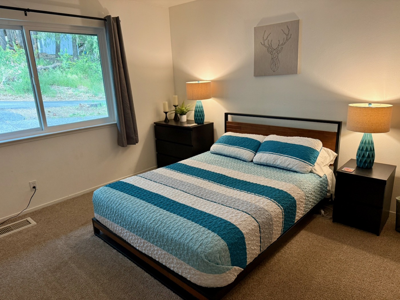 Bedroom with teal lamps, geometric deer wall art, and warm wood-frame bed