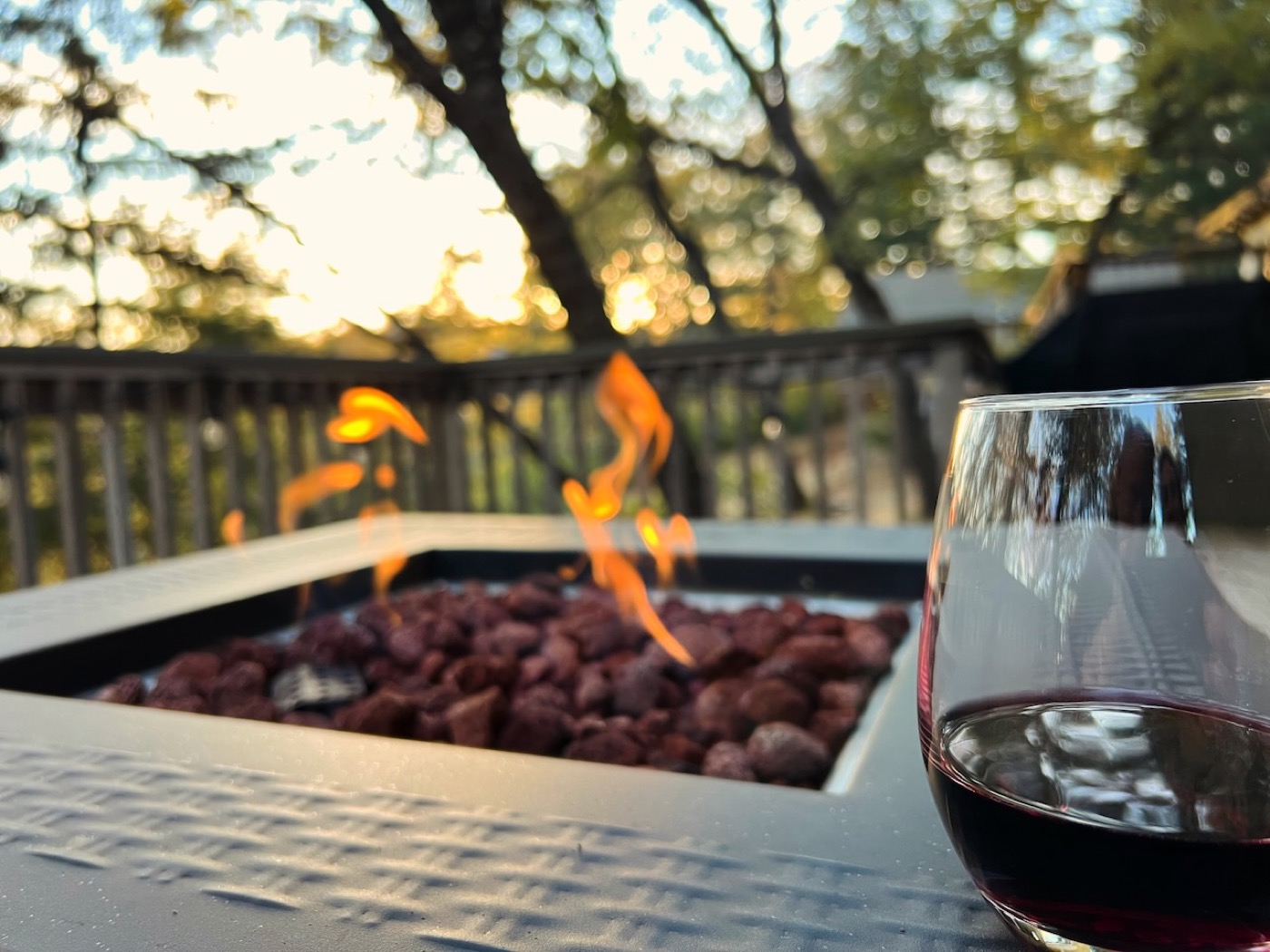 Gas fire pit glowing with lava rocks and a glass of red wine at golden hour on the deck