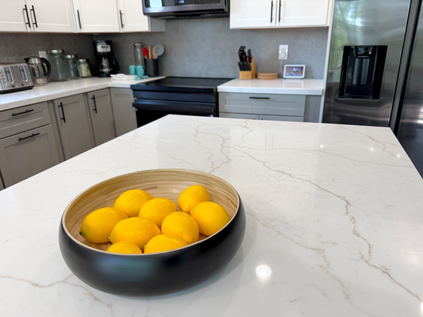 Modern kitchen with quartz waterfall island, grey shaker cabinets, and bowl of Meyer lemons